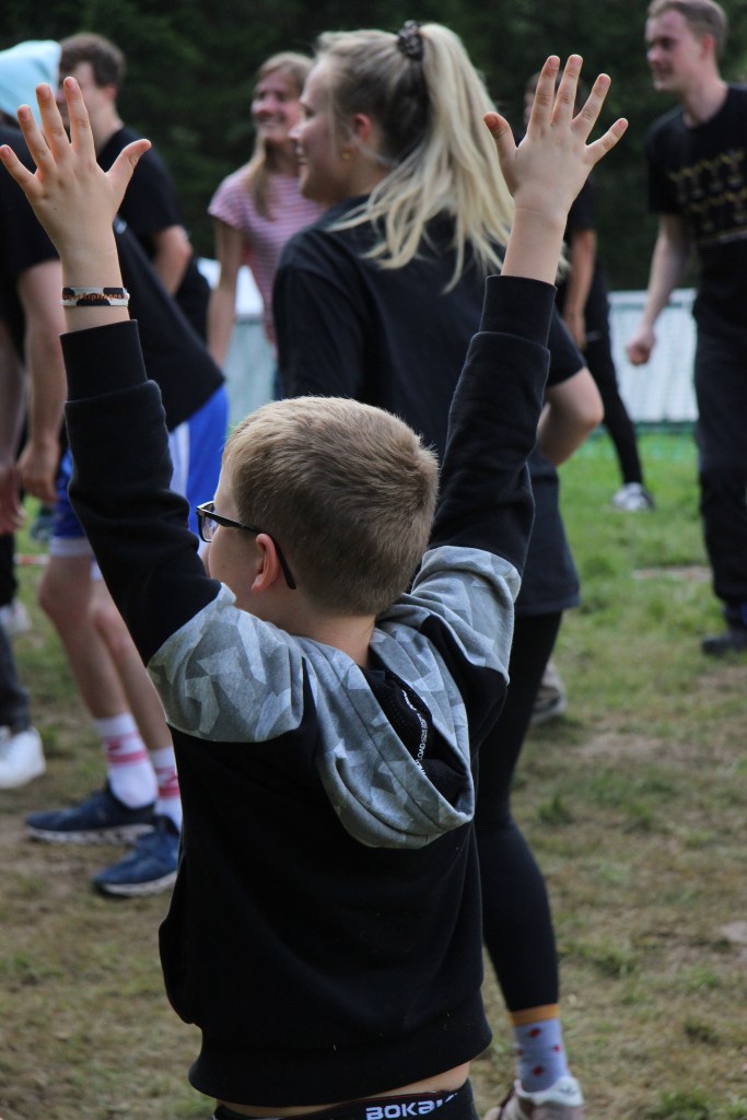 Ein Kind wirft freudig seine Arme nach oben. Im Hintergrund sind Mitarbeitende zu sehen