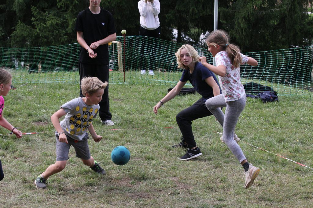 Ein Softball fliegt in der Mitte von drei Kindern, die, von der Kamera so eingefangen, in der Luft zu schweben scheinen